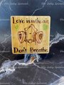 Photo of four inch wooden tile square on a clear acrylic stand infront of a black marble background. Wood has been burned with the words "Love is in the air. Don't Breathe" and has an image of a respirator breathing mask with heart shaped filters. Watercolor accents have been added.